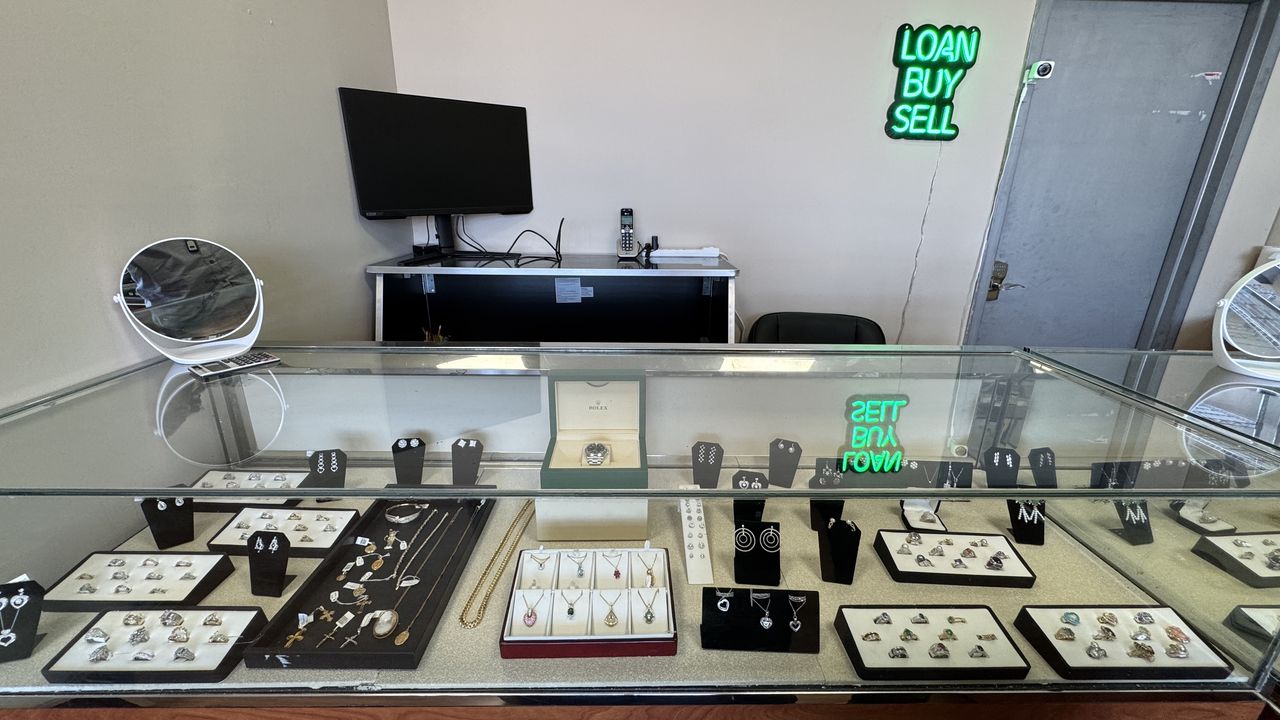 Jewelry display case with rings and necklaces beneath a Loan · Buy · Sell neon sign